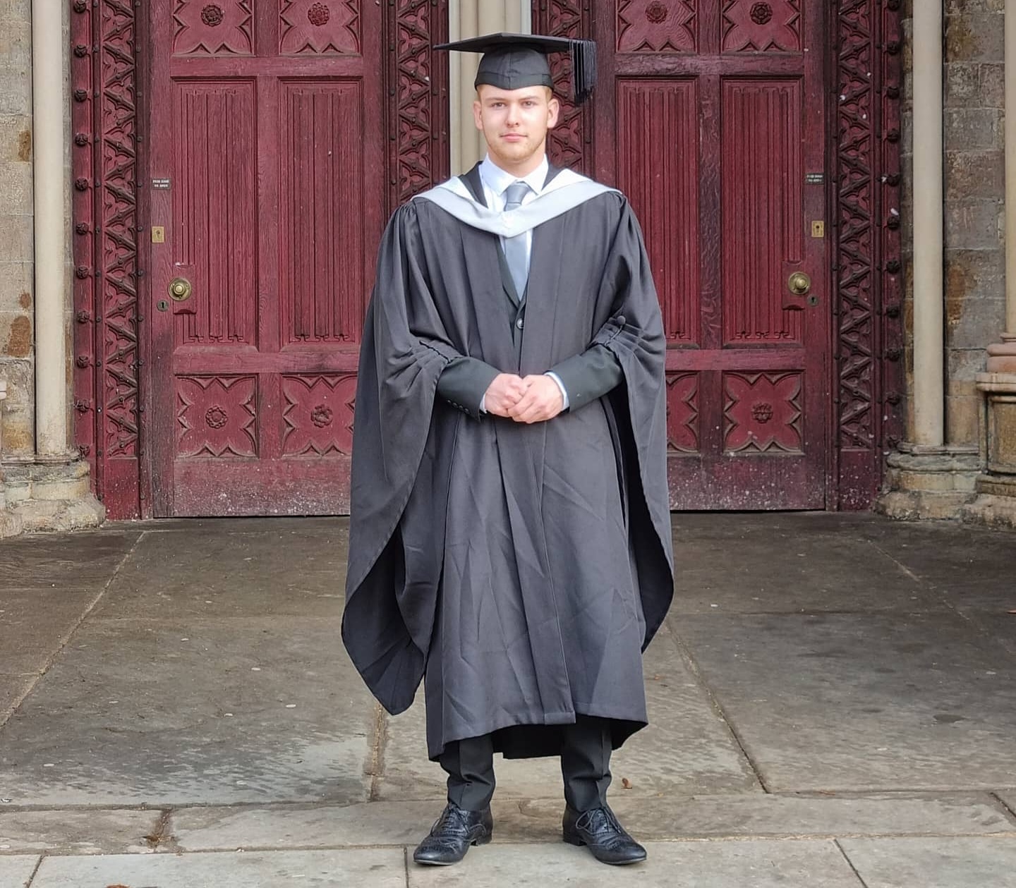 Photo of Robert standing in front of St Albans Cathedral in Graduation robes